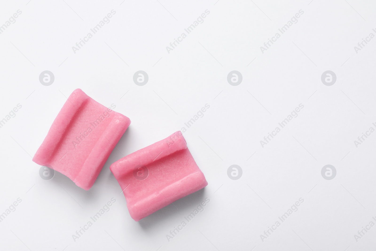 Photo of Tasty pink chewing gums on white background, flat lay. Space for text