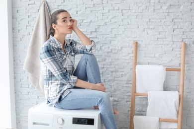 Photo of Young woman sitting on washing machine in laundry room