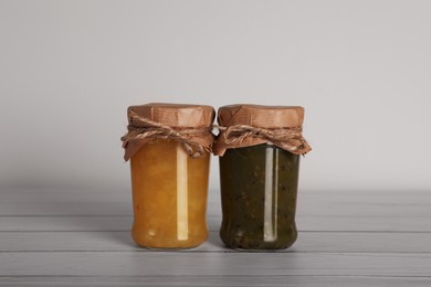 Jars with preserved fruit jams on white wooden table