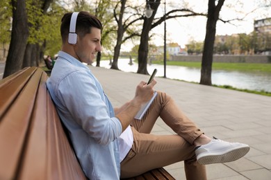 Photo of Happy man with smartphone listening to audiobook on bench near river