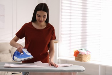 Young woman ironing clean sweatshirt at home, space for text