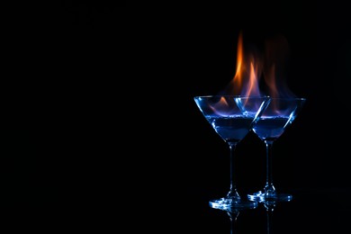 Photo of Cocktail glasses with flaming vodka on black background, space for text