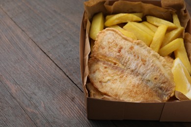 Delicious fish and chips in paper box on wooden table, closeup. Space for text