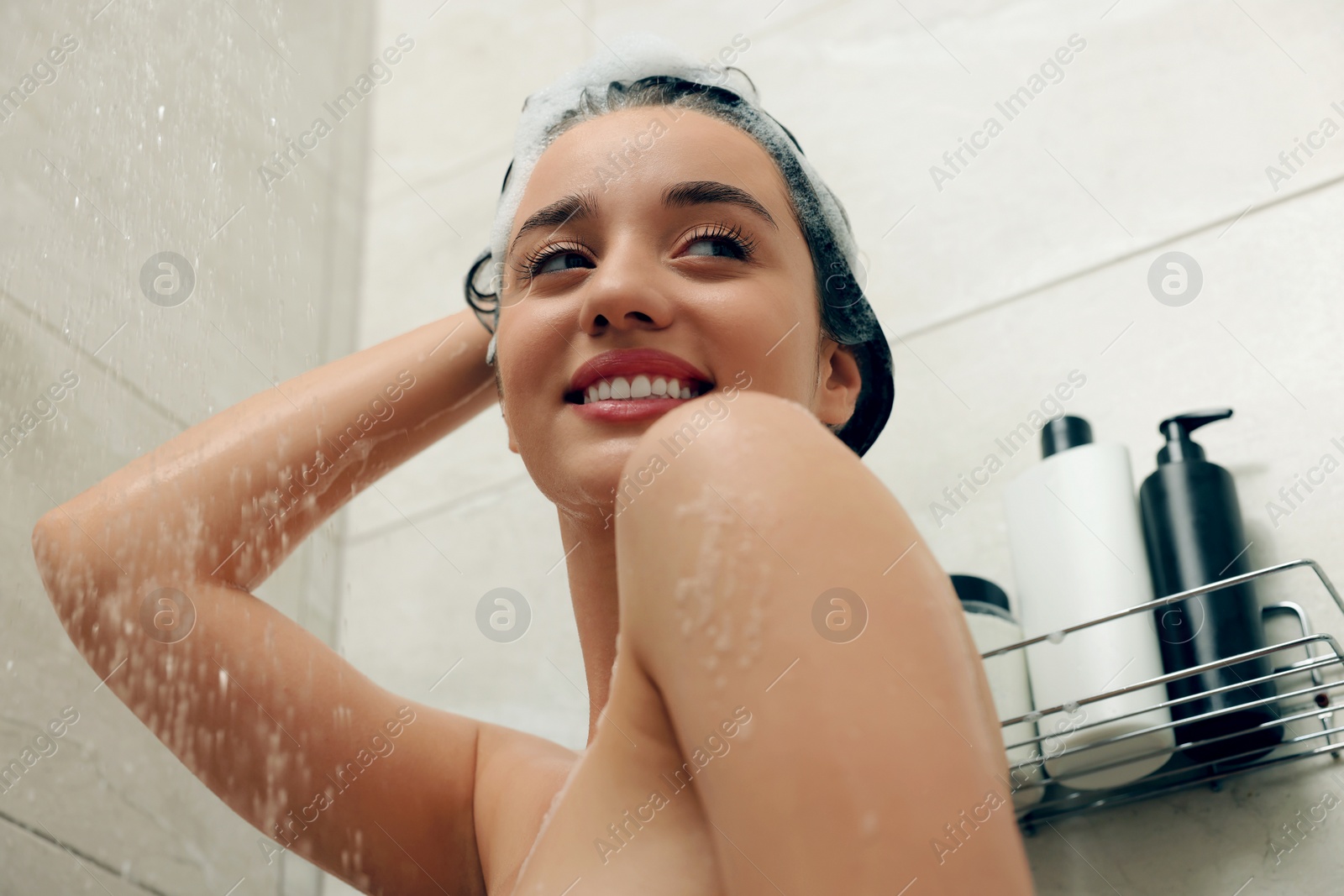 Photo of Beautiful woman washing hair in shower, low angle view