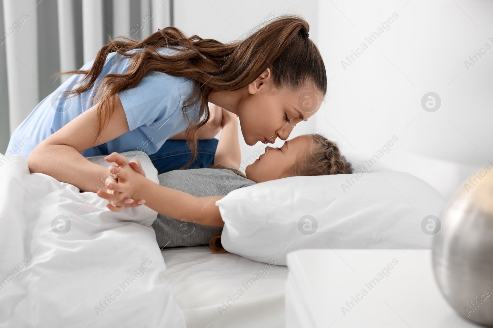 Photo of Happy mother kissing her cute daughter on bed at home