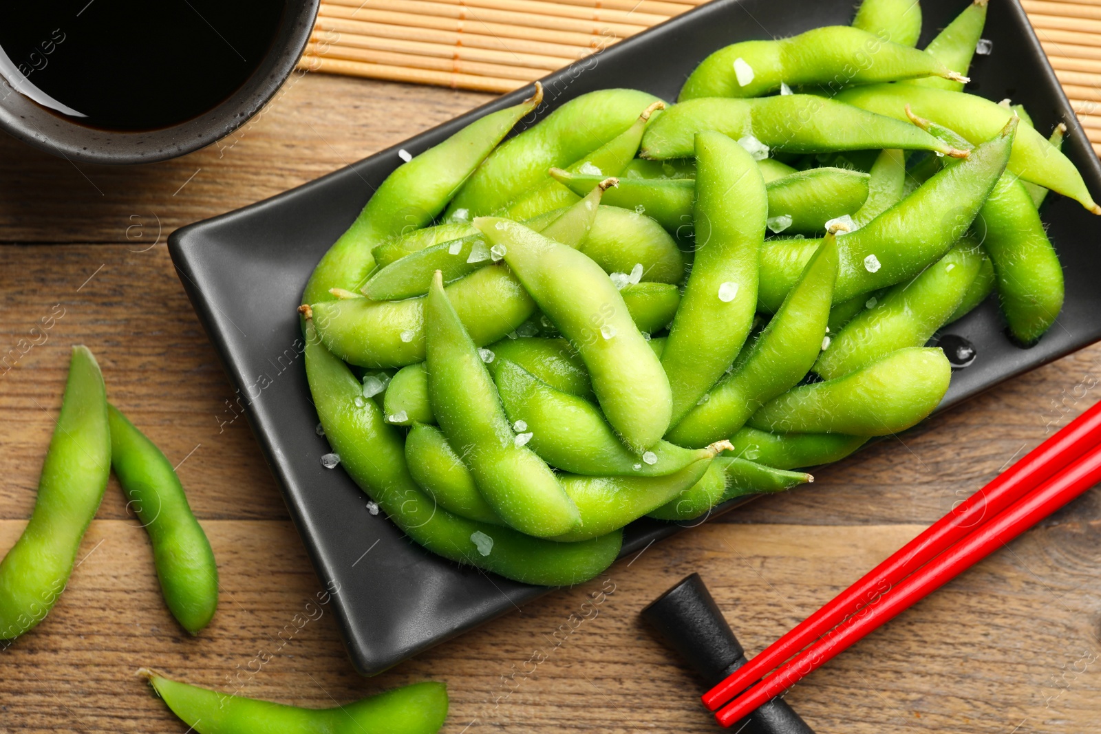 Photo of Green edamame beans in pods served with soy sauce on wooden table, flat lay