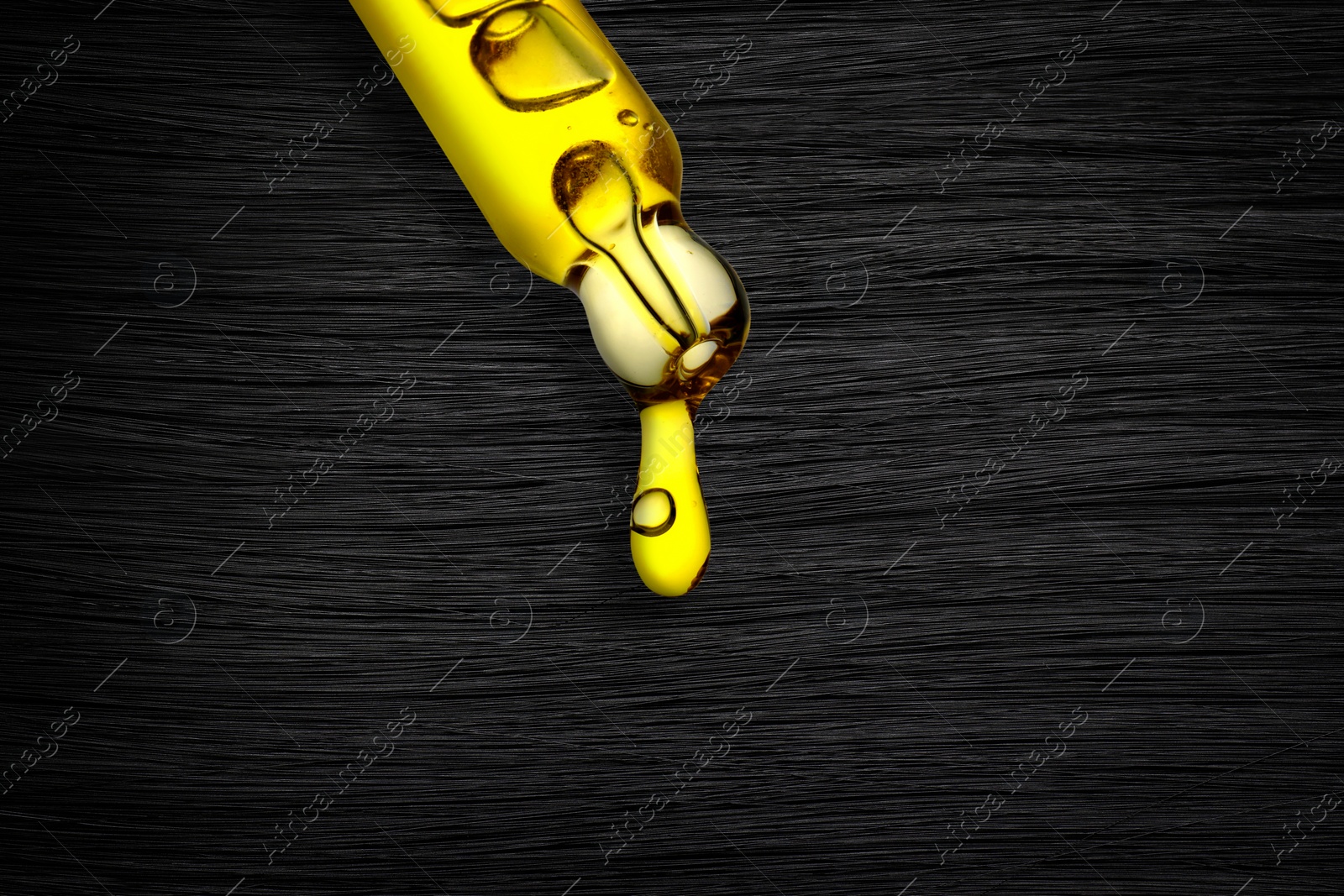 Image of Dripping cosmetic oil from pipette onto brunette hair, closeup