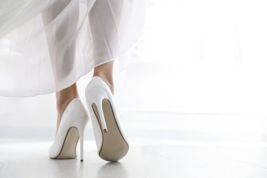 Photo of Young bride in beautiful wedding shoes walking indoors, closeup