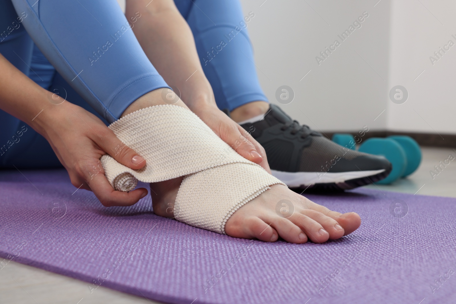 Photo of Woman wrapping foot in medical bandage on yoga mat indoors, closeup