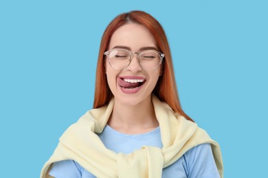 Photo of Happy woman showing her tongue on light blue background