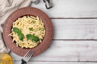 Photo of Plate of delicious trofie pasta with cheese and basil leaves on white wooden table, flat lay. Space for text