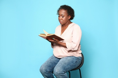 Portrait of mature African-American woman reading book on light blue background