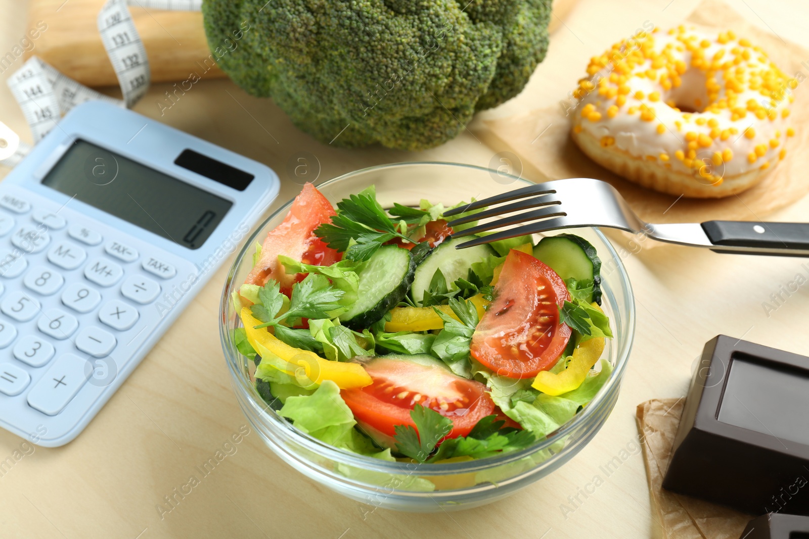 Photo of Calculator, tasty salad in bowl and other food on wooden table. Weight loss concept