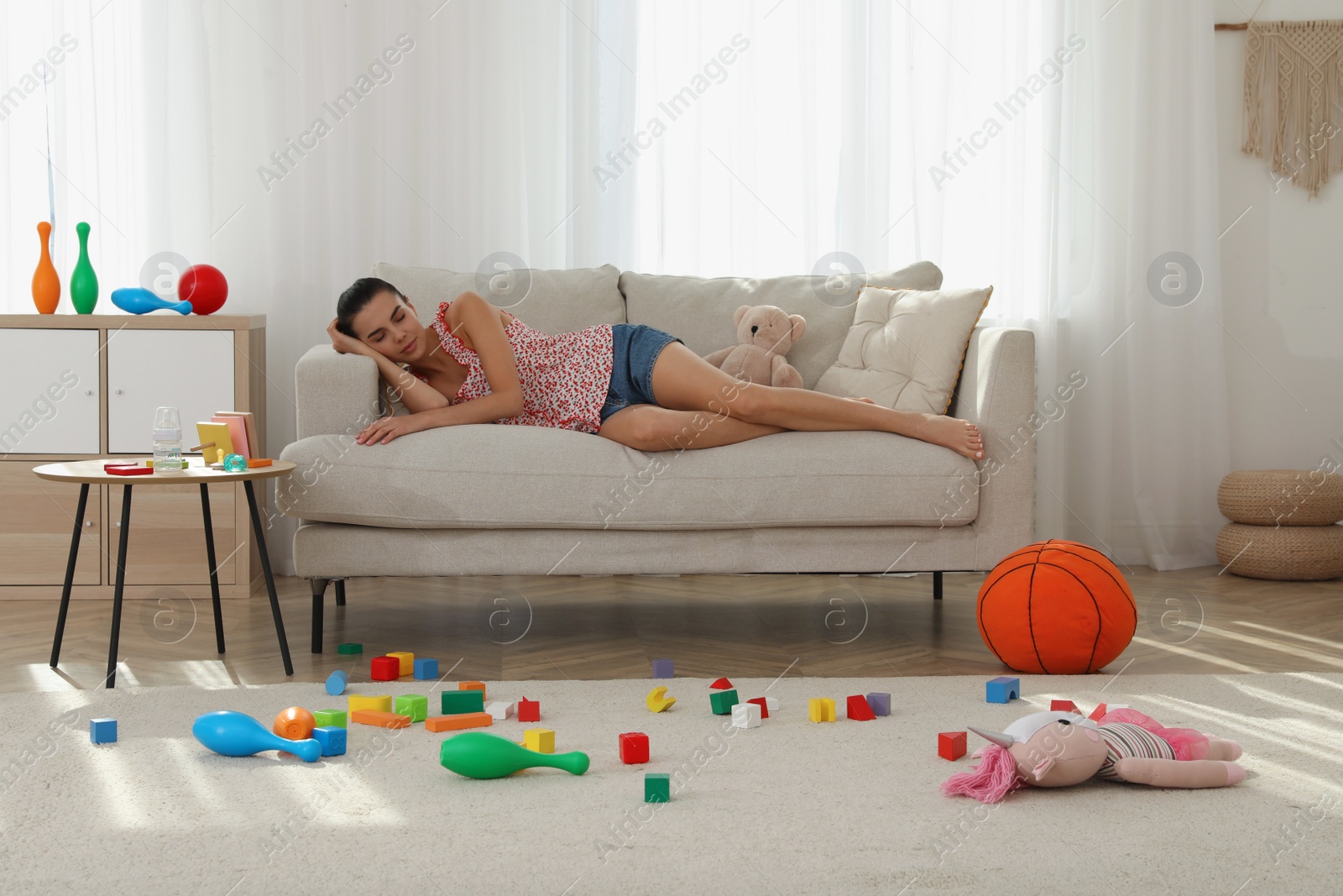 Photo of Tired young mother sleeping on sofa in messy living room