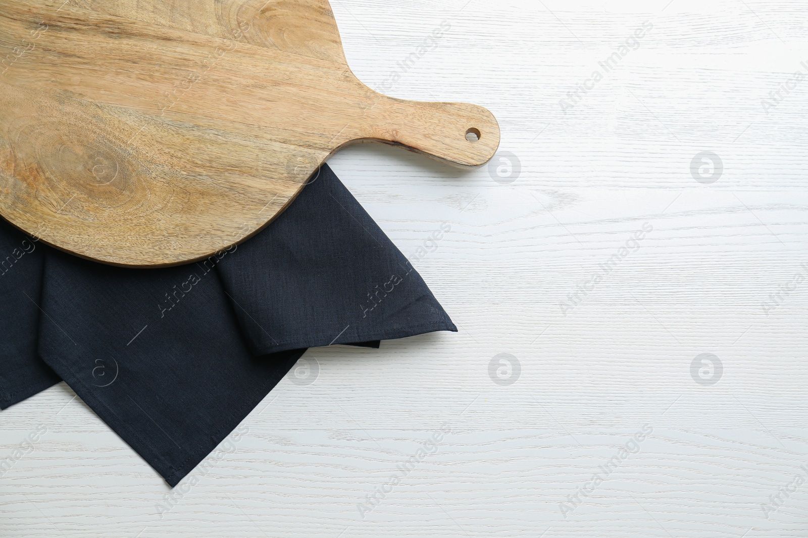 Photo of Empty wooden board and black napkin on white table, top view. Space for text