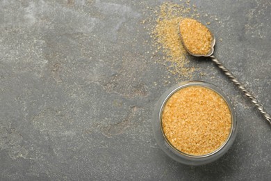 Brown sugar in bowl and spoon on grey textured table, top view. Space for text