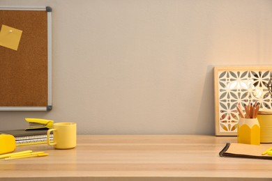 Photo of Stylish workplace with stationery on wooden desk near light wall. Interior design