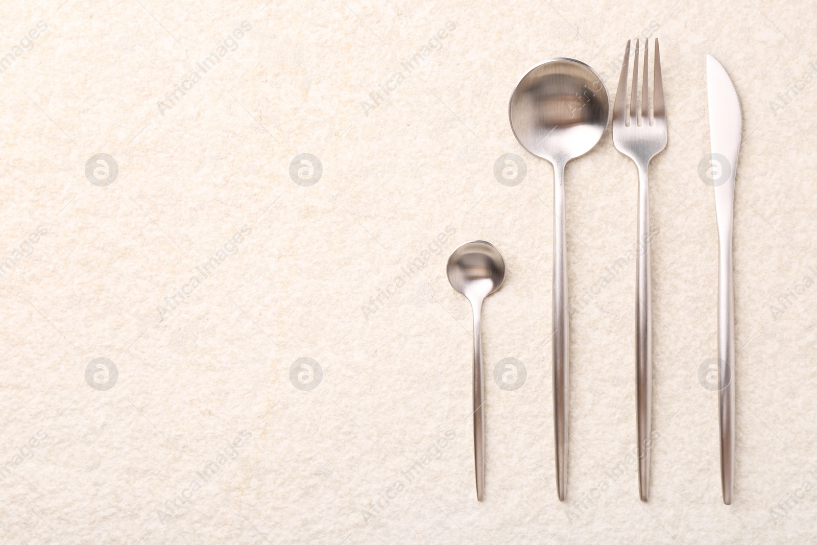Photo of Stylish silver cutlery set on light textured table, flat lay. Space for text