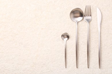 Photo of Stylish silver cutlery set on light textured table, flat lay. Space for text