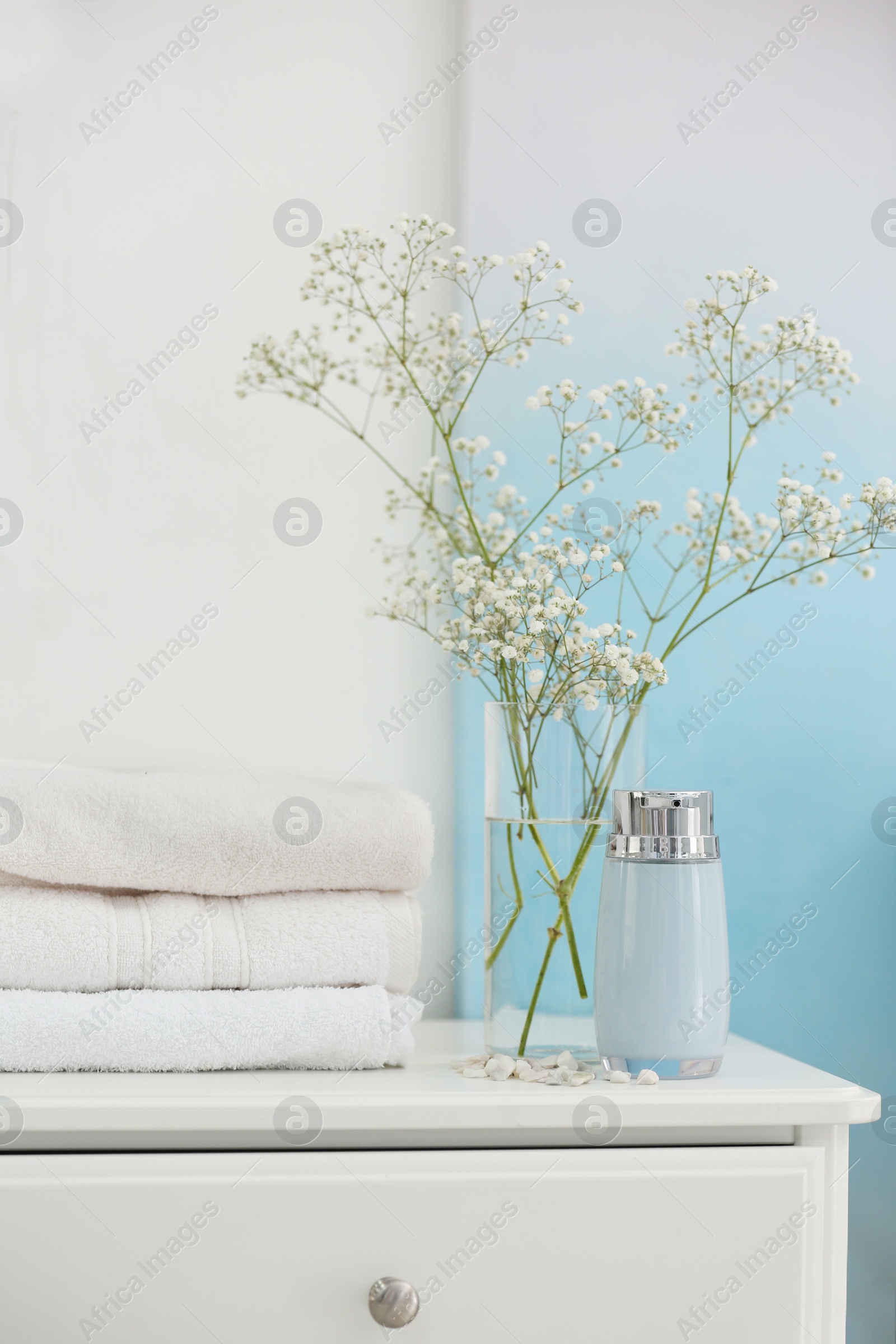 Photo of Fresh clean towels, soap dispenser and flowers on cabinet in bathroom