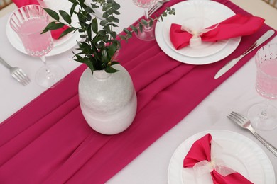 Table setting. Glasses of tasty beverage, plates, pink napkins and vase with green branches in dining room, above view