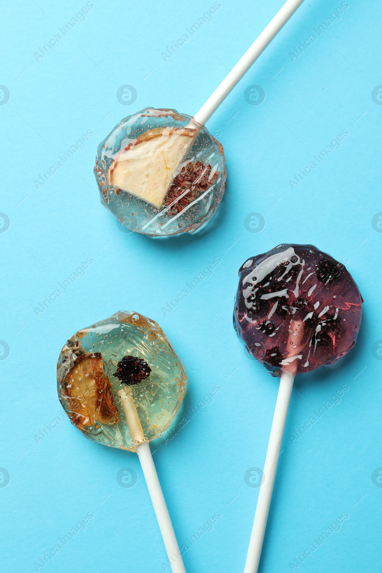 Photo of Sweet colorful lollipops with berries on light blue background, flat lay