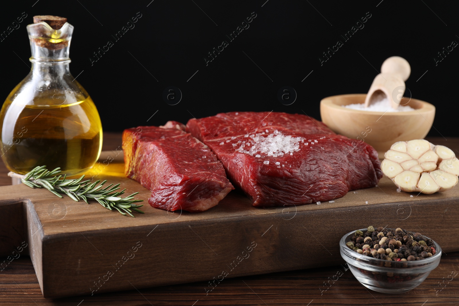 Photo of Fresh raw beef cuts with oil and spices on wooden table