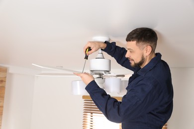 Photo of Electrician with screwdriver repairing ceiling fan indoors
