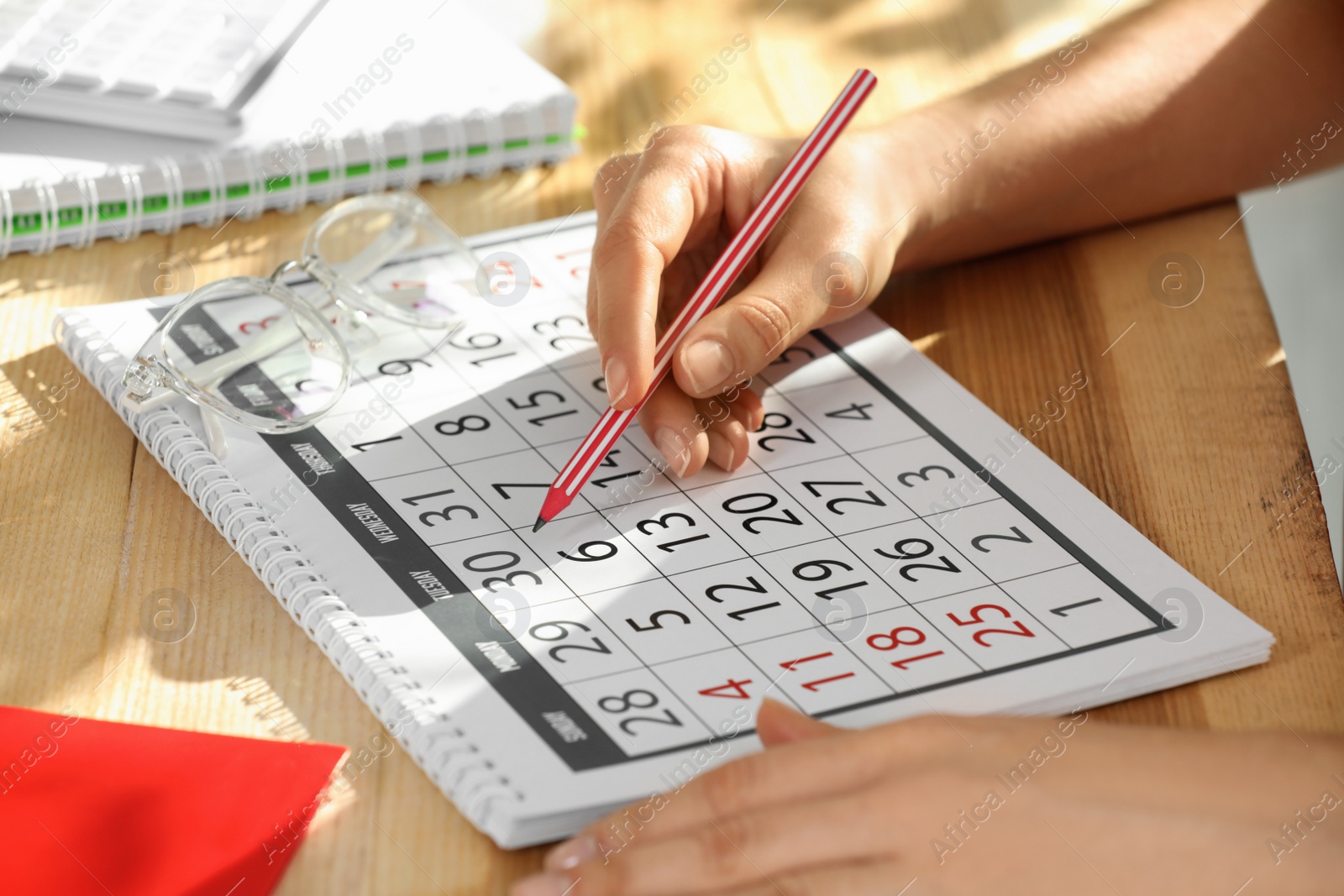 Photo of Woman marking date in calendar at wooden table, closeup