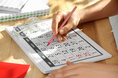 Woman marking date in calendar at wooden table, closeup