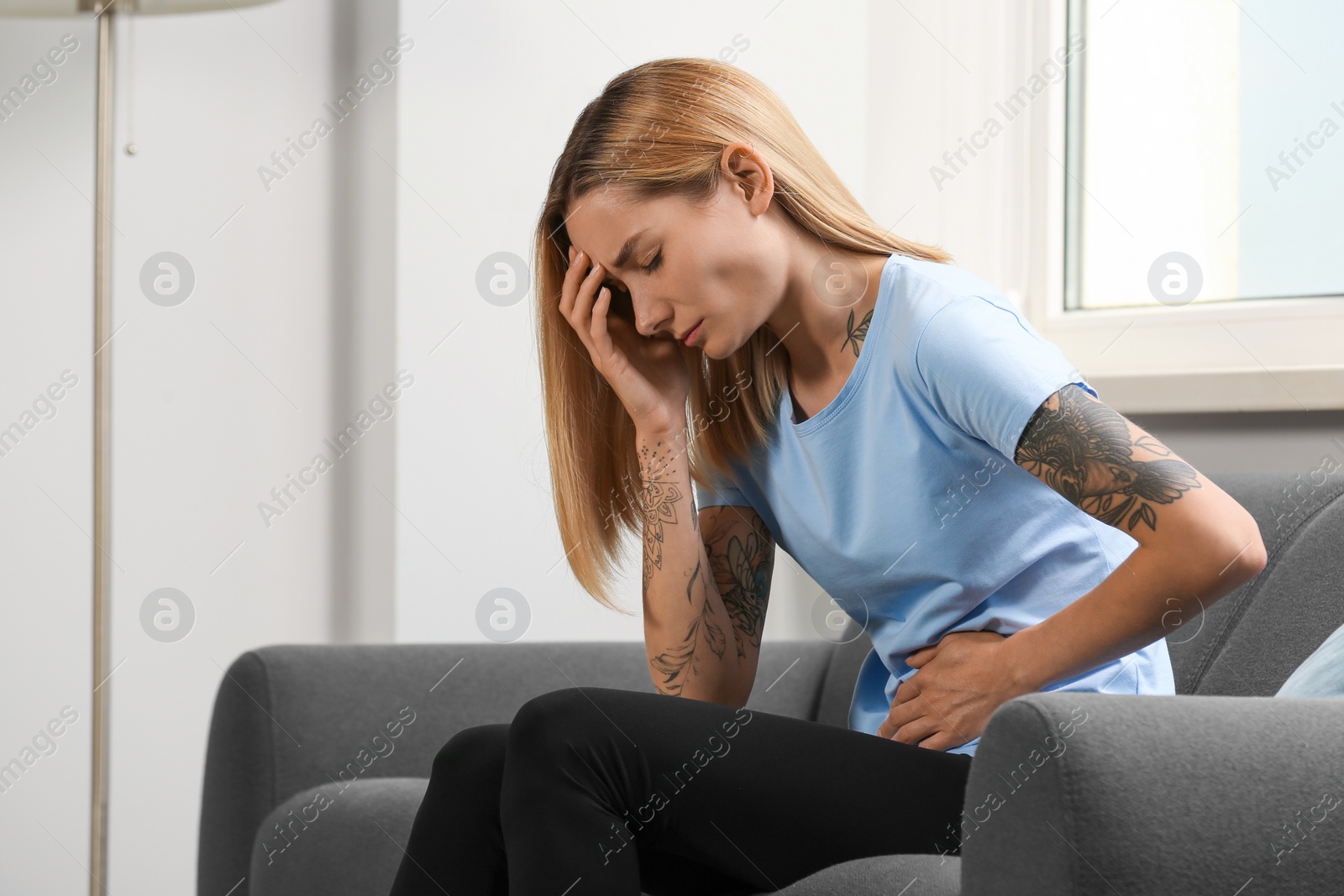 Photo of Young woman suffering from menstrual pain on sofa indoors