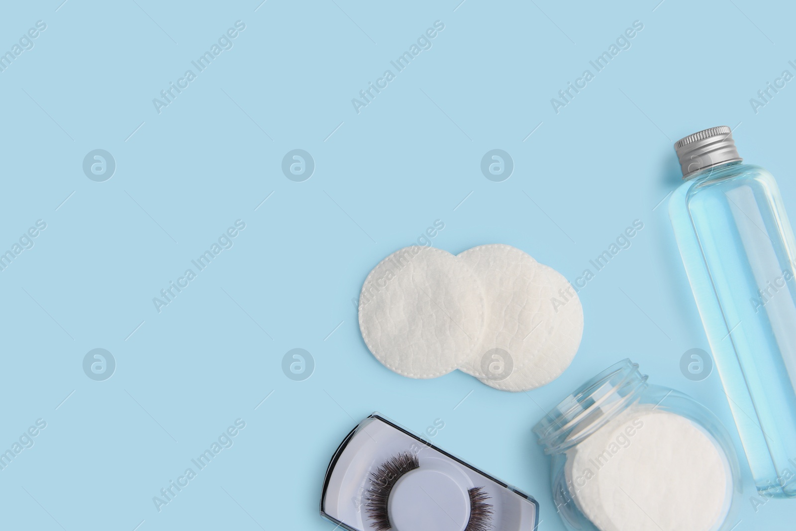 Photo of Bottle of makeup remover, cotton pads and false eyelashes on light blue background, flat lay. Space for text