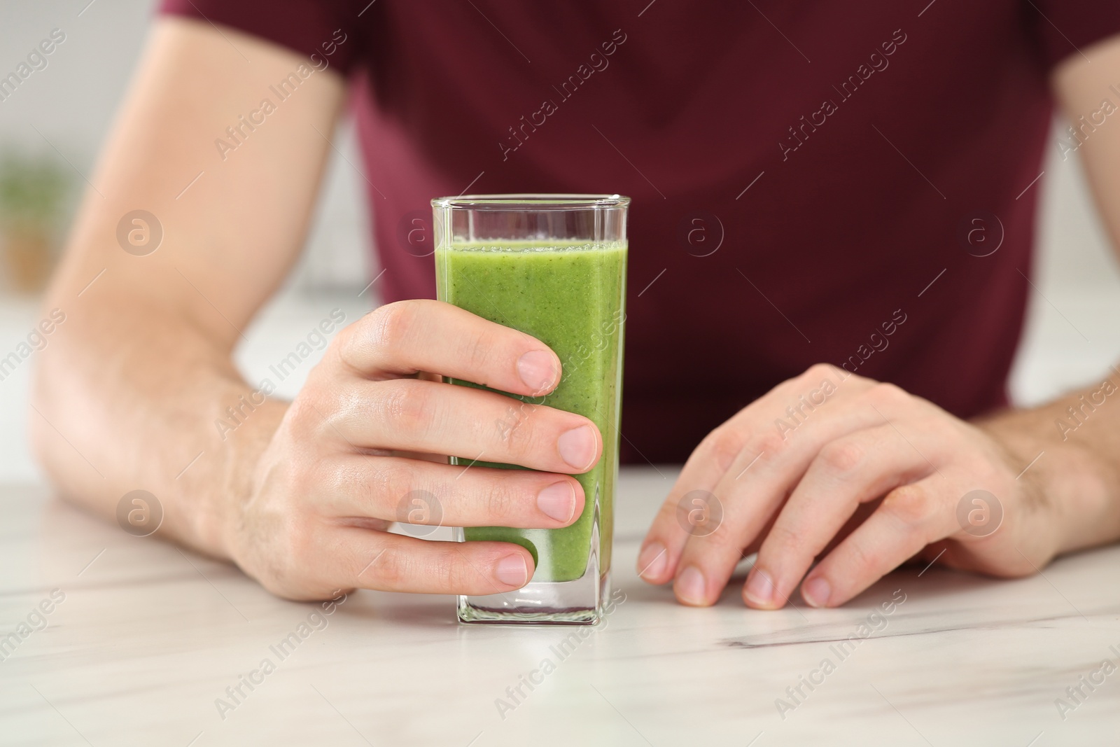 Photo of Man drinking delicious fresh smoothie at white marble table indoors, closeup