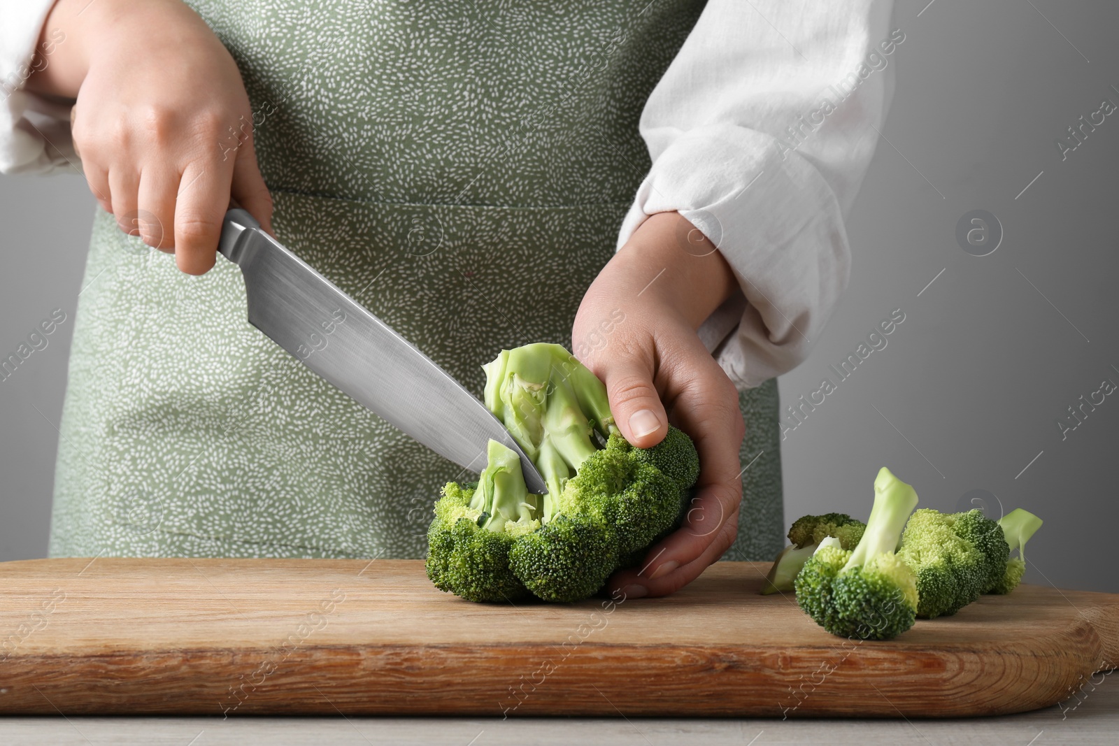 Photo of Woman cutting fresh broccoli at wooden table, closeup