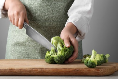 Photo of Woman cutting fresh broccoli at wooden table, closeup