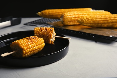 Photo of Ceramic plate with grilled corn cobs on light table