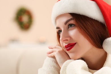 Photo of Beautiful young woman in Santa hat on blurred background, space for text. Celebrating Christmas