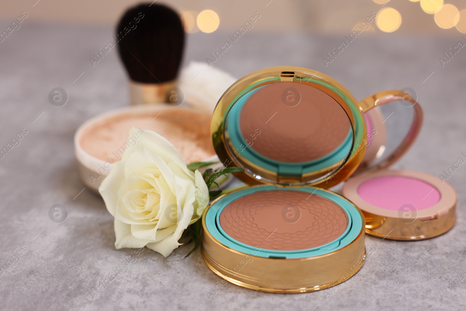 Photo of Composition with bronzer, blusher and rose flower on grey textured table, closeup