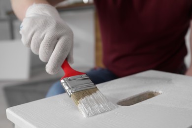 Man using brush to paint bekvam with white dye indoors, closeup
