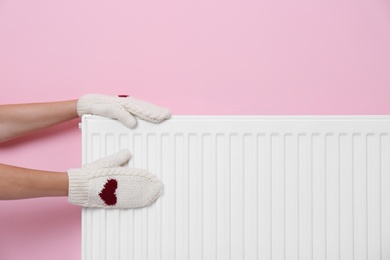 Photo of Woman in mittens touching radiator indoors, closeup. Central heating system