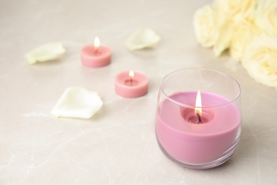 Photo of Burning candle in glass holder and roses on light table, space for text