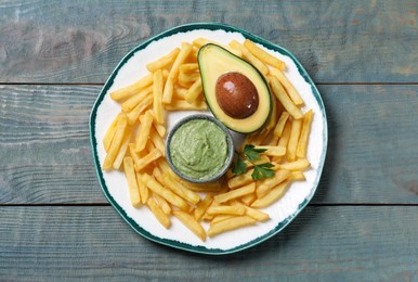 Photo of Plate with french fries, guacamole dip, parsley and avocado served on grey wooden table, top view