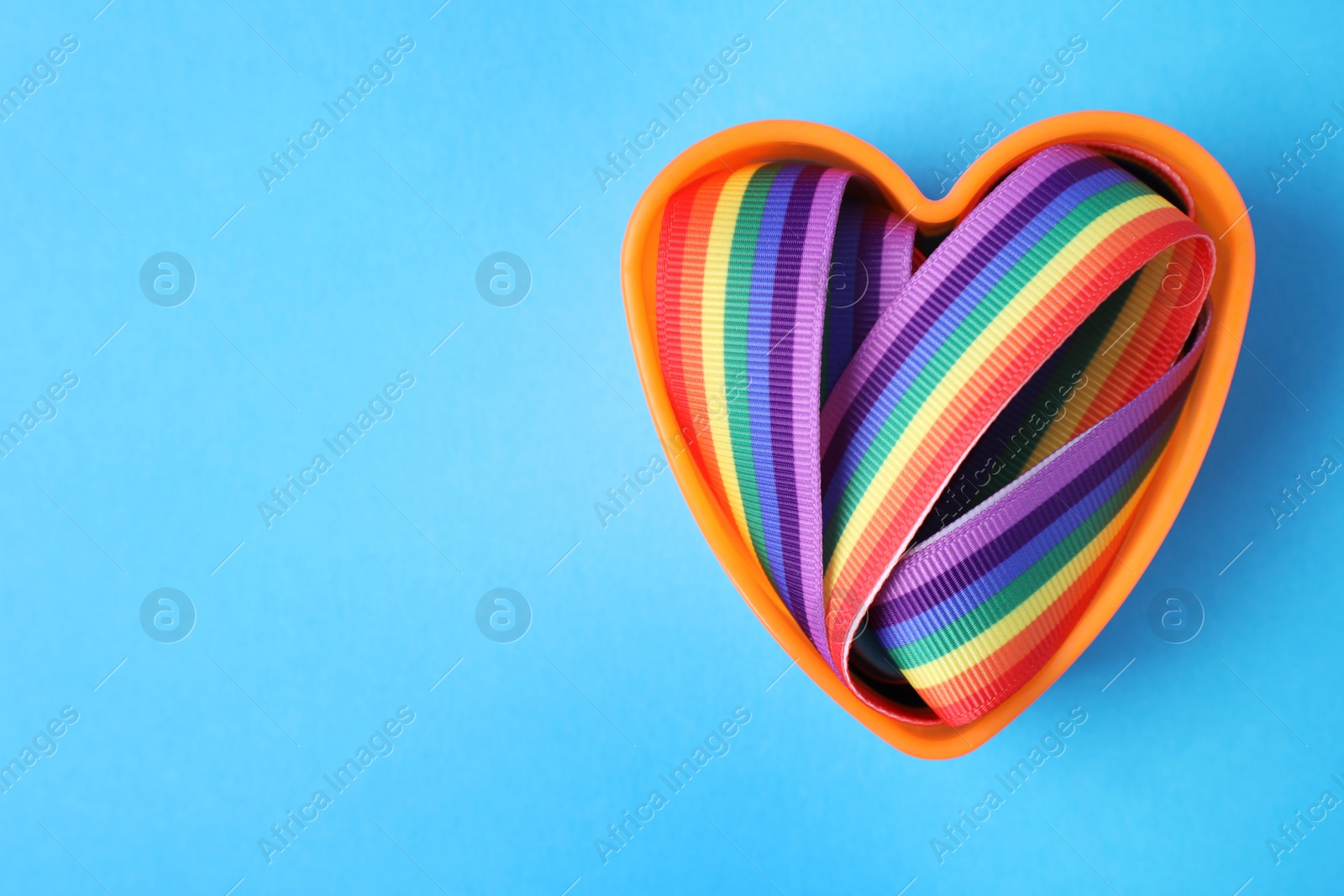 Photo of Heart shaped mold and bright rainbow ribbon on color background, top view with space for text. Symbol of gay community