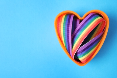 Heart shaped mold and bright rainbow ribbon on color background, top view with space for text. Symbol of gay community