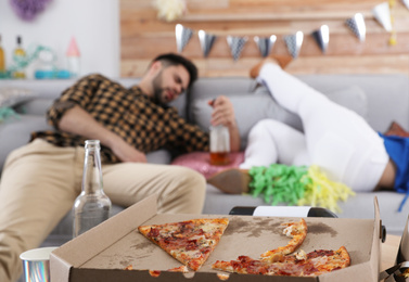 Drunk friends sleeping in messy room after party, focus on pizza