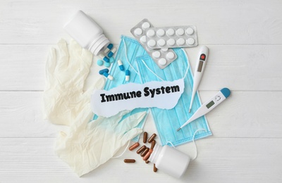 Paper piece with phrase Immune system and medical supplies on white wooden table, flat lay