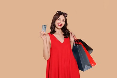 Photo of Beautiful young woman with paper shopping bags and credit card on beige background