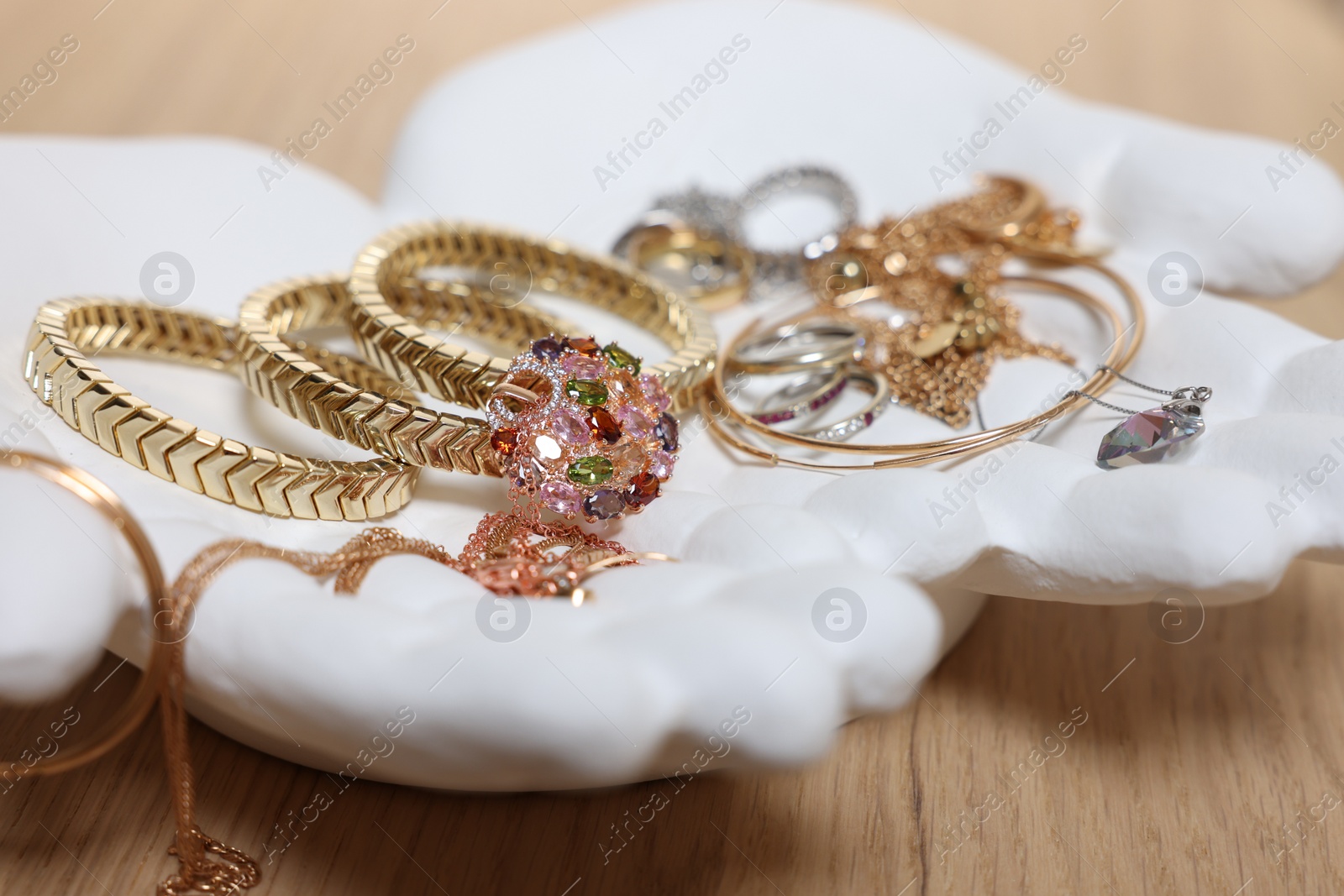 Photo of Ceramic hand stand with stylish bracelets and other accessories on wooden table, closeup