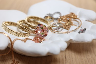 Photo of Ceramic hand stand with stylish bracelets and other accessories on wooden table, closeup