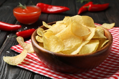 Photo of Bowl with potato chips on wooden table, closeup